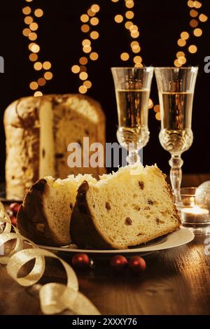 Tagliate a fette il panettone italiano, vino frizzante e decorazioni con le luci di Natale sullo sfondo Foto Stock