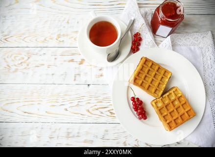 Waffle con marmellata di ribes rosso e frutti di bosco su un piatto bianco e tè su sfondo di legno Foto Stock