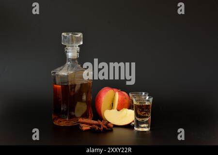 Liquore di mele con cannella e anice, forte alcol fatto in casa in due bicchieri e una bottiglia su sfondo nero. Primo piano. Foto Stock