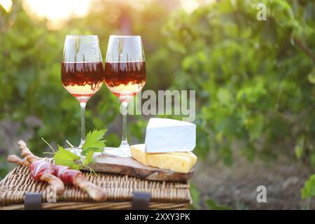 Due bicchieri di vino rosato con pane, carne, uva e formaggio sulla vigna sfondo Foto Stock