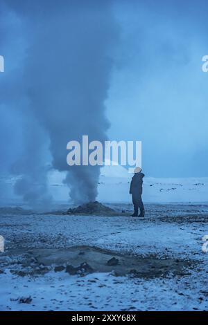 Un uomo sta nella neve guardando un grande pennacchio di fumo. Il cielo è di colore blu intenso e la neve è bianca. La scena è tranquilla e tranquilla, con Foto Stock