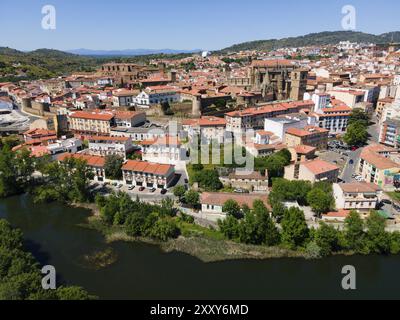 Città storica con tetti rossi e una cattedrale dominante, circondata da colline lussureggianti e un fiume in primo piano, vista aerea, Plasencia, fiume Jerte, CA Foto Stock