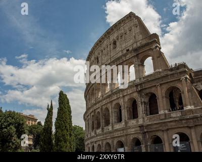 Vista laterale del maestoso Colosseo con alberi in primo piano e cielo nuvoloso, Roma, Italia, Europa Foto Stock