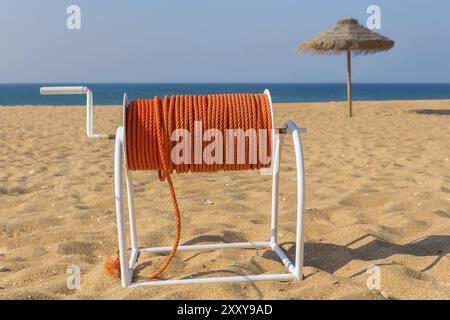 Aspo con orange fune di soccorso sulla spiaggia con ombrellone e mare Foto Stock