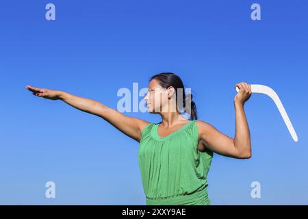 Giovane donna colombiano gettando boomerang bianco in aria blu Foto Stock