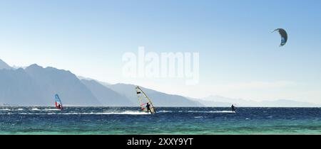 Windsurf e kitesurfer cavalcano nel Mar Rosso sullo sfondo della costa rocciosa in Egitto Dahab Foto Stock