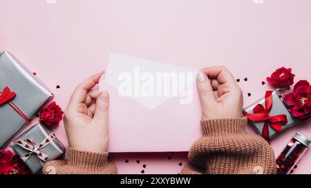 Le mani femminili tengono lettera d'amore vuoto messaggio in busta aperta, biglietto di auguri di San Valentino o invito bianco mock up. Spazio di copia, vista dall'alto. Rosa ba Foto Stock