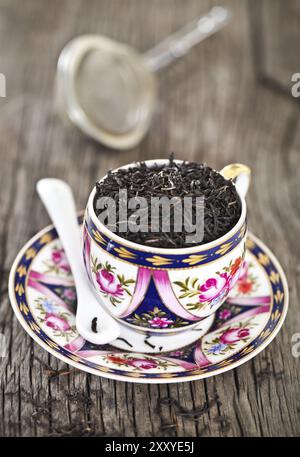 Primo piano di foglie di tè in tazza vintage. Tè nero Foto Stock