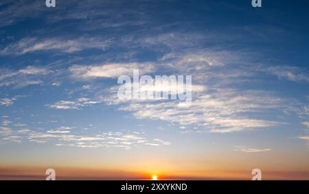 Cielo colorato al tramonto con sole tramontare dietro nuvole di colore arancione e giallo Foto Stock