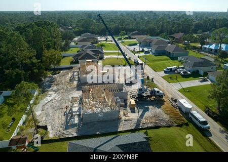 Gru di sollevamento camion e costruttori che lavorano sulla costruzione di tetti di casa residenziale incompiuta con struttura a telaio in legno nella zona suburbana della Florida. Ho Foto Stock