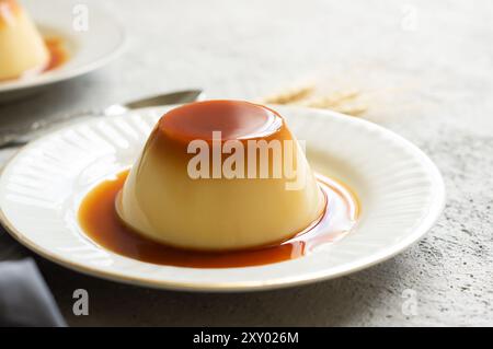 Budino di crema al caramello con salsa al caramello nel piatto su un tavolo rustico bianco Foto Stock