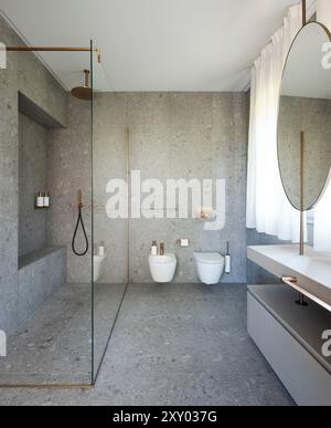 Bagno moderno con grandi lastre di granito, sia alle pareti che al pavimento. Vista frontale del WC, del bidet e dell'ampia doccia in vetro. Nessuno dentro Foto Stock