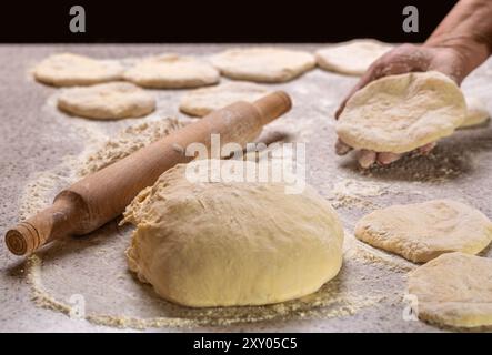 Processo di preparazione delle torte. Cuocere a casa. Pasta fatta in casa per torte nelle mani delle donne. Donna che stende l'impasto sul tavolo della cucina, da vicino. Cottura delle mani Foto Stock