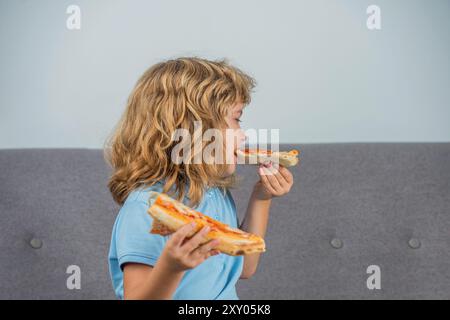 Ritratto di un bambino bellissimo si gode una deliziosa fetta di pizza, piace questo gusto. Il ragazzo ama mangiare la pizza. Il bambino mangia una fetta di pizza al peperoni Foto Stock