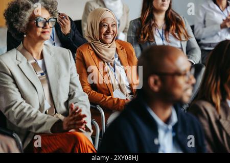 Un gruppo eterogeneo di professionisti, tra cui una donna musulmana sorridente, che partecipa a una conferenza d'affari e ascolta una presentazione. Foto Stock