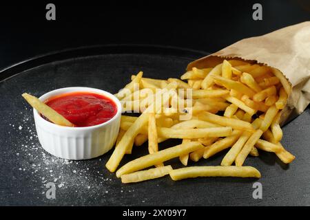 Una porzione di patate e ketchup su sfondo scuro. Fast food, primo piano Foto Stock