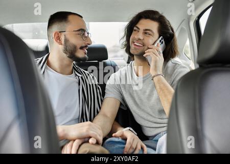 Una coppia gay sul sedile posteriore di un'auto, una al telefono, l'altra che guarda con affetto. Foto Stock