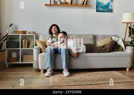 Due uomini si stanno rilassando su un divano, uno tiene il telefono e l'altro lo guarda. Foto Stock