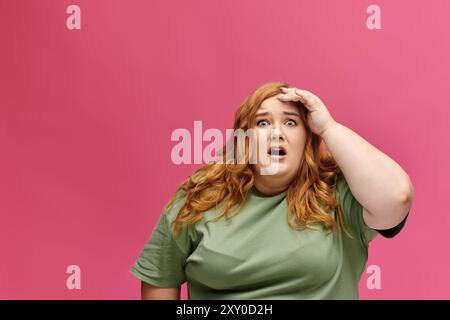 Una donna taglia Plus con una camicia verde sembra scioccata su uno sfondo rosa. Foto Stock