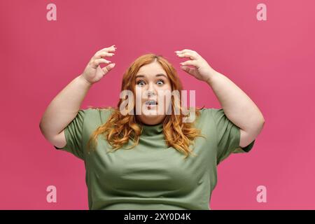 Rossa curvata in tee verde, mani sollevate in caso di shock Foto Stock