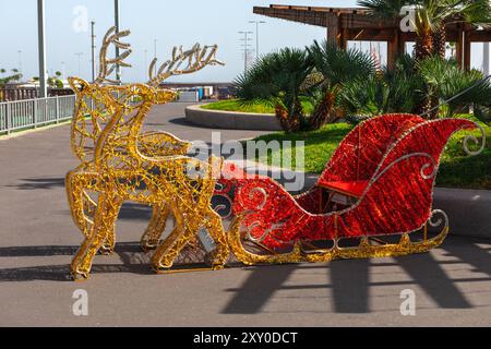 La slitta rossa con due cervi è seduta su un marciapiede. La slitta e' decorata con luci d'oro e rosse ed e' una decorazione festosa. Reindeer st Foto Stock