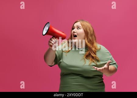 Una donna con lunghi capelli rossi e una camicia verde regge un megafono e grida. Foto Stock