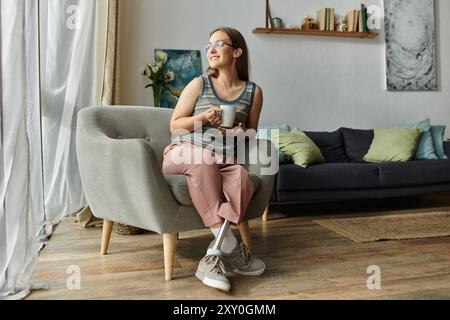 Una donna con una gamba protesica gode di una bevanda calda nel suo salotto mentre la luce del sole filtra attraverso la finestra Foto Stock