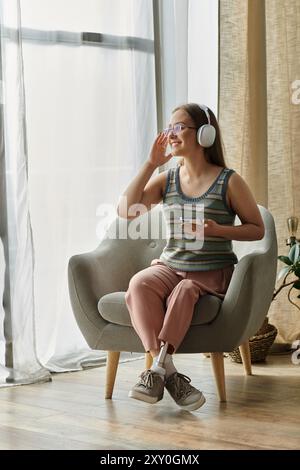 Una giovane donna con una gamba protesica siede in un salotto moderno, ascoltando musica con le cuffie. Foto Stock