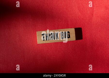 Pensa a un grande messaggio scritto su un blocco di legno con sfondo rosso. Un grande simbolo del pensiero concettuale. Copia spazio. Foto Stock