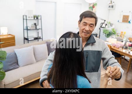 Coppie di anziani che ballano in un accogliente soggiorno con arredamento moderno e illuminazione calda Foto Stock