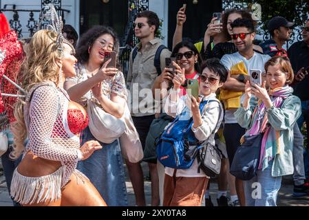 Turisti pubblici che fotografano una ballerina al Notting Hill Carnival Grand Parade 2024. Giornata degli adulti il lunedì festivo. Foto Stock