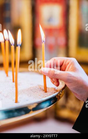 Primo piano delle mani di un prete cattolico che colloca una candela accesa in un portacandele durante un servizio ad Altea, Valencia, Spagna. Foto Stock