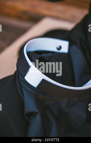 Ravvicinato e irriconoscibile di un sacerdote cattolico, vestito nero e distintivo collare bianco, fotografato in una chiesa di Altea, Valenc Foto Stock