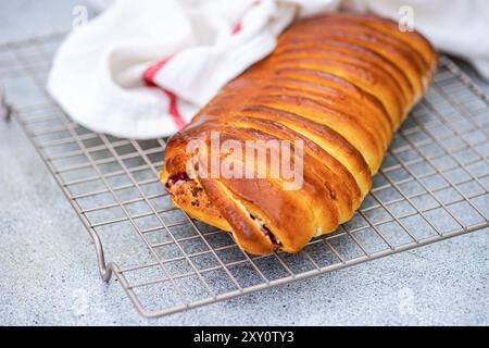 Brioche appena sfornata ripiena di ciliegia e formaggio fresco su una griglia rinfrescante, luccicante con una crosta dorata. Foto Stock