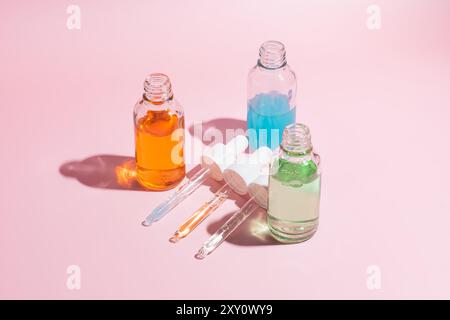 Vista dall'alto di tre flaconi contagocce per siero vibranti con pipette su sfondo rosa pastello, che mostrano prodotti di bellezza e dermocosmesi. Foto Stock