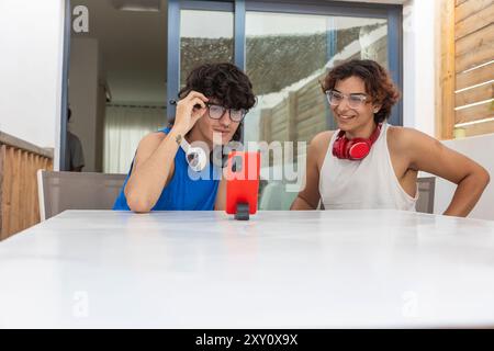 Una giovane coppia gay si diverte a vicenda mentre guarda un telefono, condividendo un'interazione gioiosa in un ambiente familiare informale Foto Stock