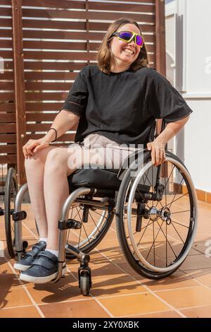 Una donna gioiosa in sedia a rotelle, che indossa occhiali da sole e un top nero, trasuda fiducia e positività all'aperto questa immagine cattura il tema dell'accesso Foto Stock