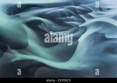 Questo scatto aereo cattura le trame ipnotiche di un fiume glaciale sulla costa meridionale dell'Islanda, mostrando una miscela di blu ghiacciato e ombre scure Foto Stock