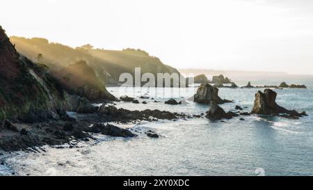 Una tranquilla scena costiera durante il tramonto con un soffice bagliore su affioramenti rocciosi e acque calme. Foto Stock