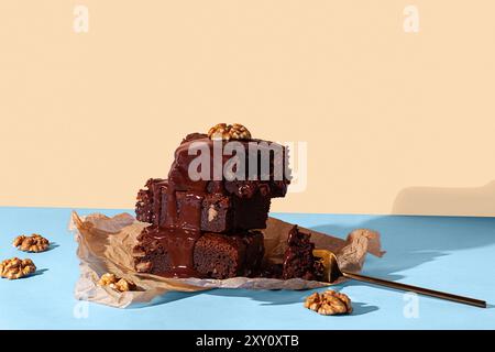 Un'allettante esposizione di brownie al cioccolato fatti in casa impilati e conditi con una ricca e lucida salsa al cioccolato e noci, presentati su un blu a contrasto Foto Stock