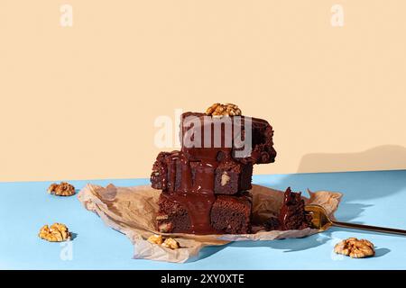 Un'allettante esposizione di brownie al cioccolato fatti in casa impilati e conditi con una ricca e lucida salsa al cioccolato e noci, presentati su un blu a contrasto Foto Stock