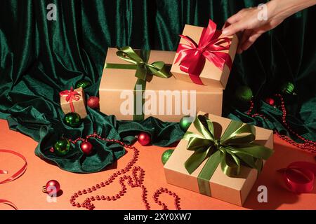 Una mano aggiunge un fiocco rosso vivace a un regalo avvolto, sullo sfondo di lussureggianti velluti verdi e ornamenti natalizi, la scena cattura lo spirito di fe Foto Stock