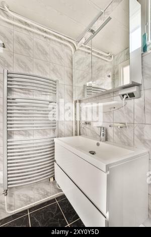 Bagno elegante e moderno con piastrelle in marmo, box doccia in vetro e elegante lavandino bianco con lavabo rettangolare. Foto Stock