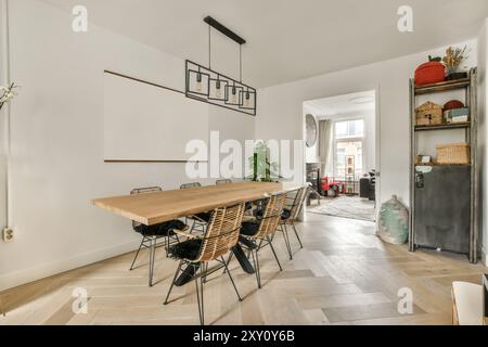 Un'ariosa sala da pranzo presenta un lungo tavolo in legno, sedie in vimini e un'esclusiva lampada sospesa, con decor minimalista e porta aperta per un livin Foto Stock