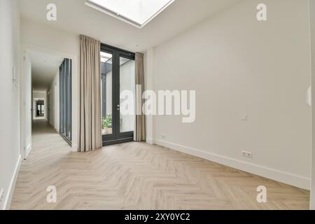 Un corridoio moderno e arioso caratterizzato da pavimento in parquet a spina di pesce, lucernario ed eleganti tende accanto a porte in vetro. Foto Stock