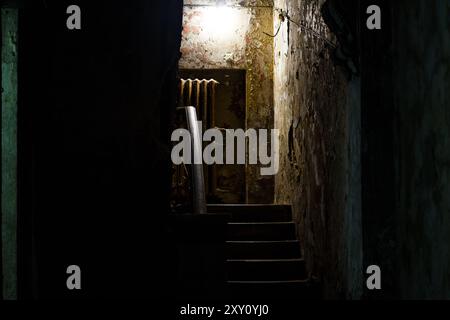 Esci dal seminterrato per le scale in un vecchio edificio cupo, esplorando case abbandonate Foto Stock