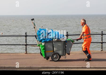 Inghilterra, Kent, Herne Bay, Seafront Promenade Street Cleaner con traboccanti cestini Foto Stock