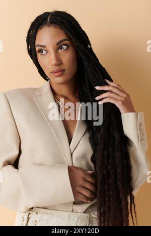 Una giovane donna con lunghe trecce nere posa in un blazer crema. Foto Stock