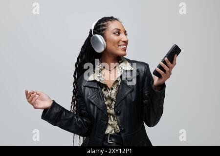 Una giovane donna con una giacca in pelle nera e una camicia con stampa animale balla e sorride tenendo il telefono. Foto Stock