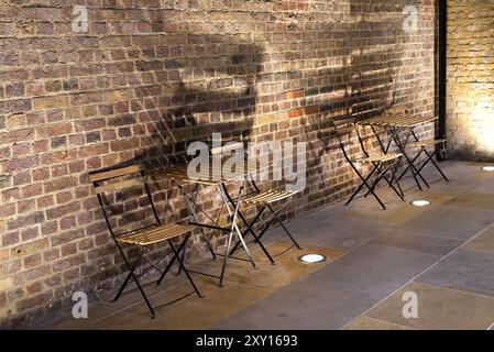 Due tavoli in legno e sedie di un caffè contro una parete di mattoni con luci che creano ombre Foto Stock